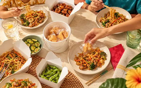 Illustration of a dinner table of takeout where a hand picks a wrapped fortune cookie from a white pail.